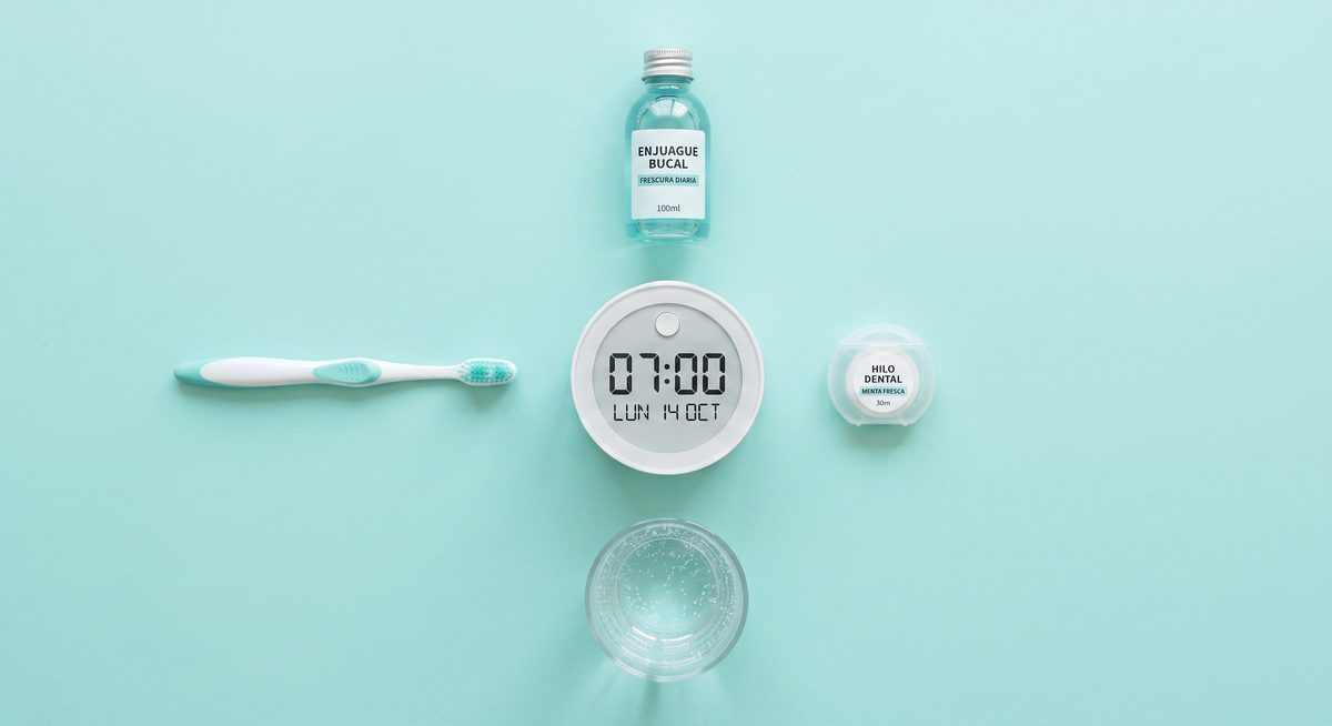 Cepillo, enjuague, hilo dental y vaso de agua alrededor de un reloj que marca 07:00